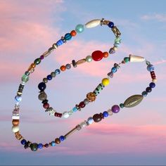 a multicolored beaded necklace hanging in the air with a pink sky behind it