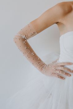 a woman in a white dress with her hands on her hips wearing gloves and pearls