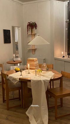 a dining room table set for two with white linens and candles on the table