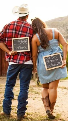 a man and woman walking down a dirt road with signs in their hands that read, i love you