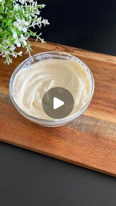 a wooden cutting board topped with a bowl filled with white sauce next to a potted plant