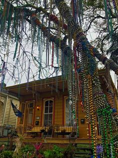 a tree with beads hanging from it's branches in front of a yellow house