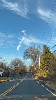 an empty street with power lines and houses in the background under a blue sky filled with wispy clouds