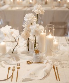 the table is set with white flowers, candles and napkins for an elegant dinner