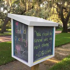 a chalkboard sign with writing on it in front of some grass and trees at the park