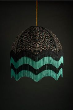 a black and green lamp hanging from a gold colored chain with fringes on it