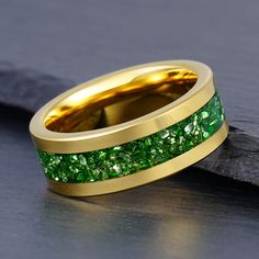 a gold ring with green stones in it on top of a black stone slabd surface