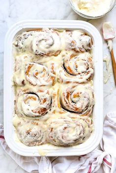 a pan filled with cinnamon rolls on top of a table next to a bowl of cream cheese