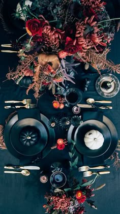 the table is set with black plates, silverware and red flowers on top of it