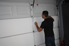 a man in black shirt and jeans working on a garage door with white paneling