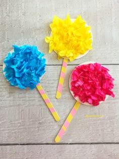 three colorful paper flowers sitting on top of a wooden table next to each other,