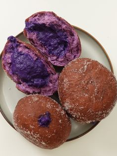 three donuts on a plate with purple powdered sugar and sprinkles