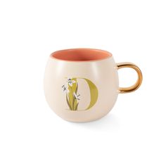 a coffee cup with a gold handle and white flowers on the side, sitting in front of a white background