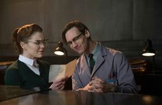 a man and woman sitting at a bar looking at something on the table in front of them