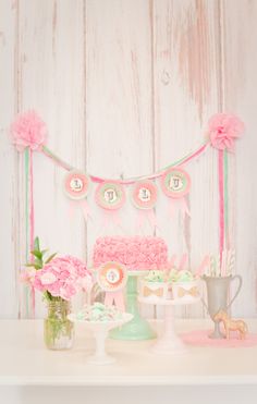 a table topped with cake and cupcakes covered in pink frosted icing