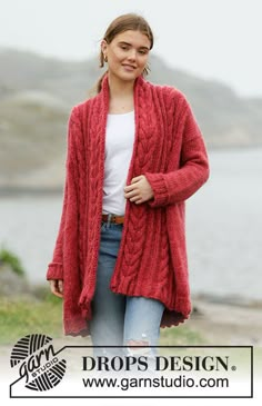 a woman wearing a red cardigan standing next to the water with her hands in her pockets