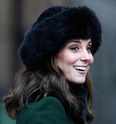 a woman wearing a fur hat and green coat smiling at the camera with her eyes closed