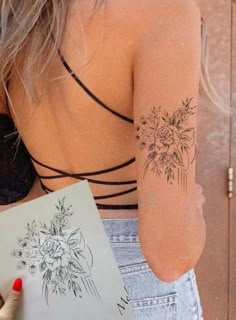 a woman is holding a drawing book with flowers on her arm and the back of her body