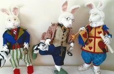 three stuffed rabbits dressed in colorful clothing and hats, one holding a cane while the other holds a bag