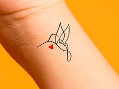 a small tattoo on the wrist of a woman's arm with a hummingbird holding a red heart