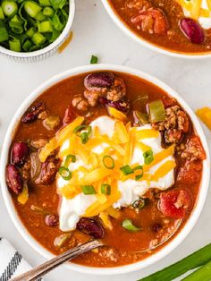 two bowls of chili soup with cheese and sour cream on the top, one bowl is full