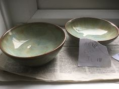 two bowls sitting on top of a newspaper next to a piece of paper with writing