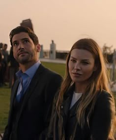 a man and woman standing next to each other in front of some people on the grass