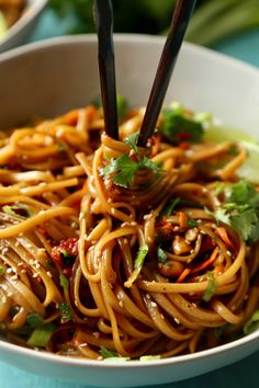 a bowl of noodles with chopsticks in it on a blue table cloth next to some vegetables