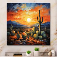 a painting on the wall of a living room with a cactus and sunset in the background