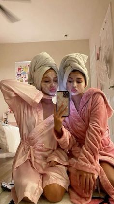 two women in pink robes sitting on the floor taking a selfie with their cell phone