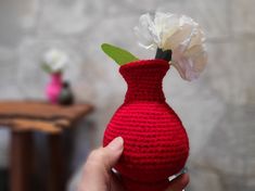 a crocheted red vase with a white flower in it is being held by a hand