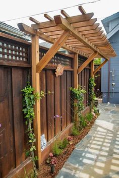 a wooden pergoline with plants growing on it and a walkway leading to the back door