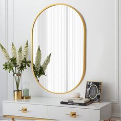 a white dresser topped with a mirror next to a vase filled with flowers and plants