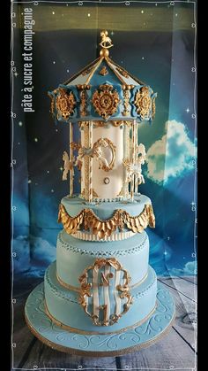 a three tiered blue cake with gold trimmings and a carousel on top