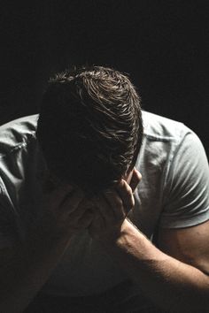 a man sitting in the dark holding his hands to his face