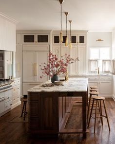 a large kitchen with white cabinets and wooden floors is pictured in this image, there are stools at the center of the island