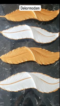 three gold and white feathers on a black marble surface with the words dekormodm above them