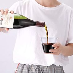 a person pouring wine into a glass with a bottle in it and another hand holding a cup