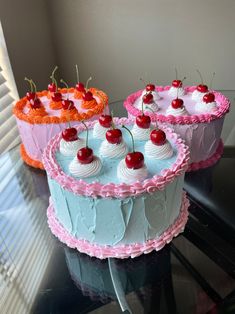 three cakes sitting on top of a table covered in frosting and cherry toppings