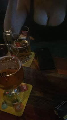 a woman sitting at a table with two glasses of beer in front of her and cell phone on the table