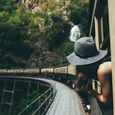 a woman wearing a hat looking out the window at a train going by on tracks