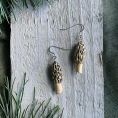 a pair of leopard print earrings hanging from a pine branch on top of a piece of wood