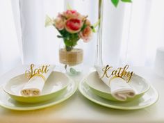 two plates with napkins on them sitting on a table next to a vase filled with flowers