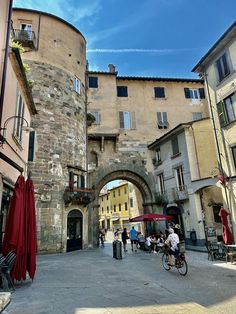 people are walking and riding bicycles in an old city street with stone buildings on either side