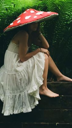 a woman wearing a red and white hat sitting on top of a wooden bench next to ferns