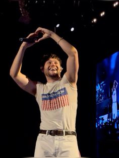 a man is holding his hands up in the air while singing into a microphone on stage