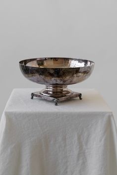 a large metal bowl sitting on top of a white table cloth covered table with an iron stand