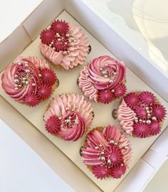 four cupcakes in a box with pink icing and flowers on them,