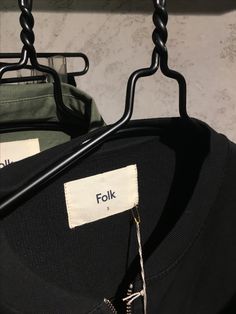 two black shirts hanging on clothes hangers next to each other with white tags reading folk