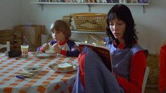 two people sitting at a table with food and drinks in front of them, one reading a book